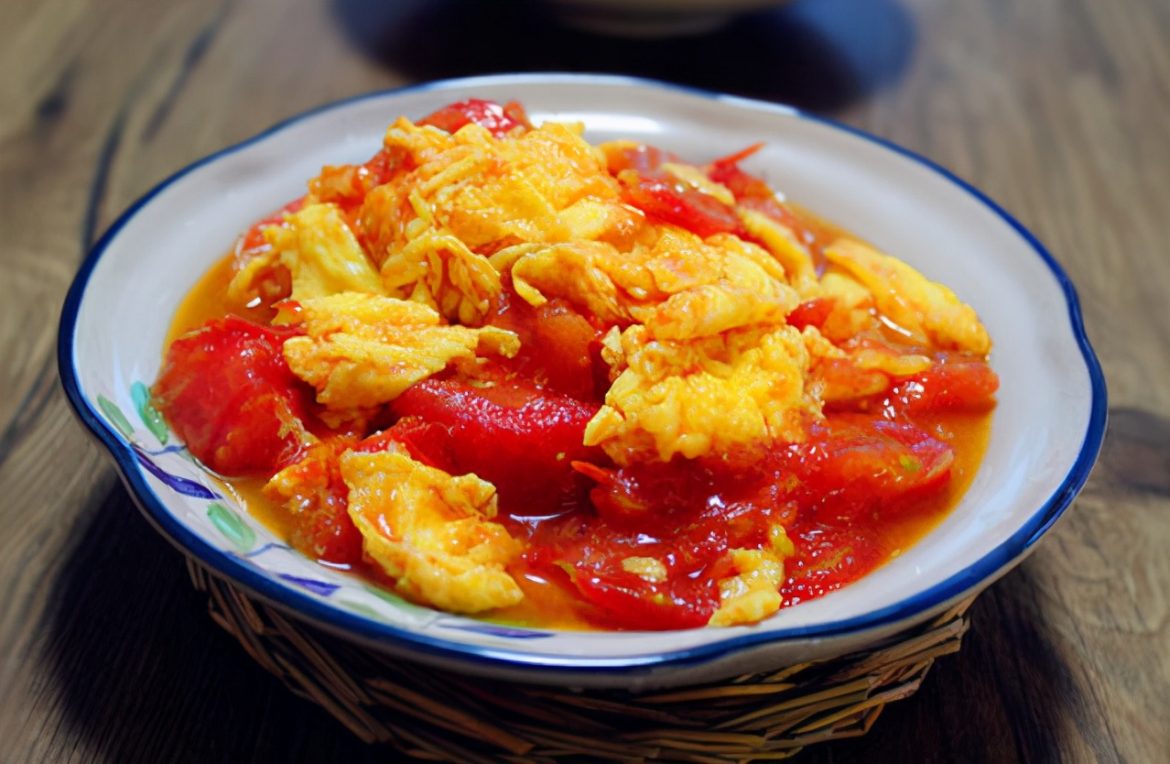 Plat de sauté d'œufs aux tomates à la chinoise (Xi Hong Shi Chao Ji Dan) avec des morceaux d'œufs moelleux et une sauce rouge onctueuse, parsemé de ciboule.