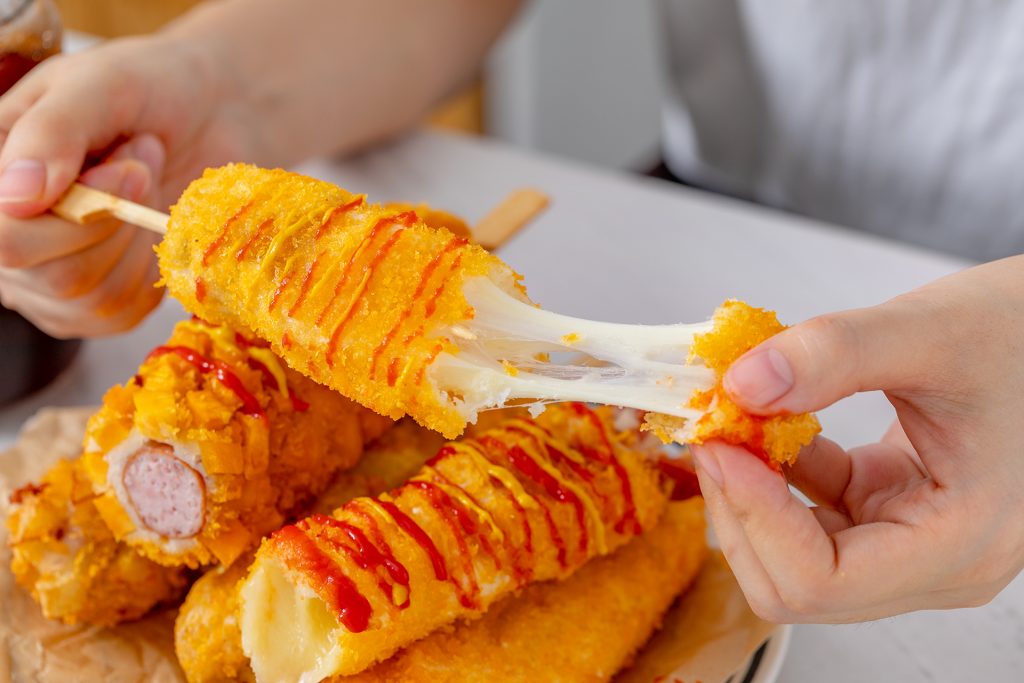 Texture fondante de la mozzarella étirée à l'intérieur d'un corn-dog coréen surgelé après cuisson au four.